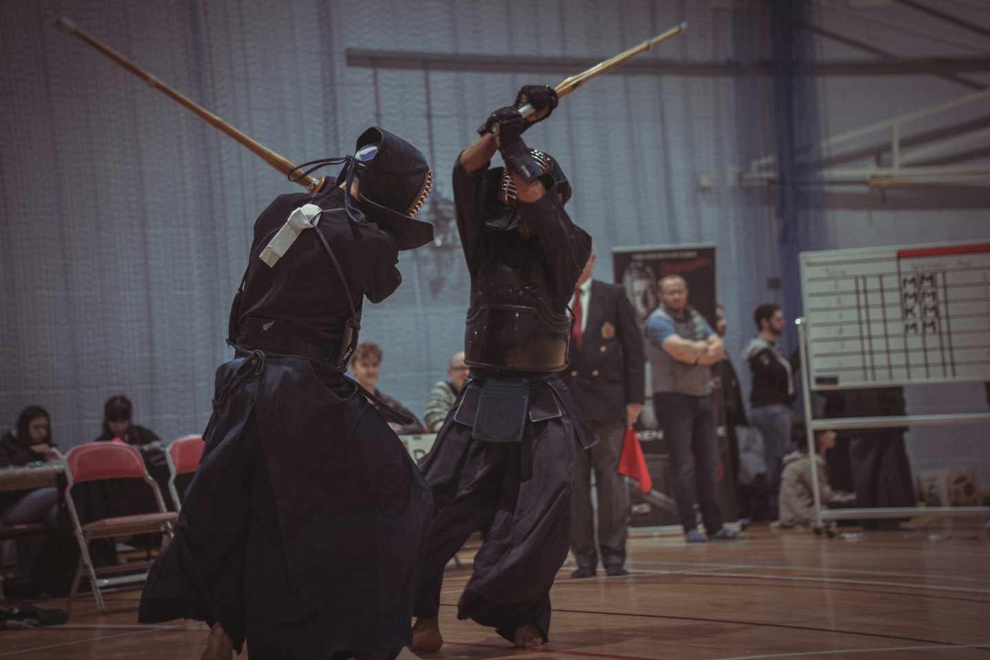 Zwei Kendo-Kämpfer in Rüstung während eines Kampfes auf einem Holzboden.