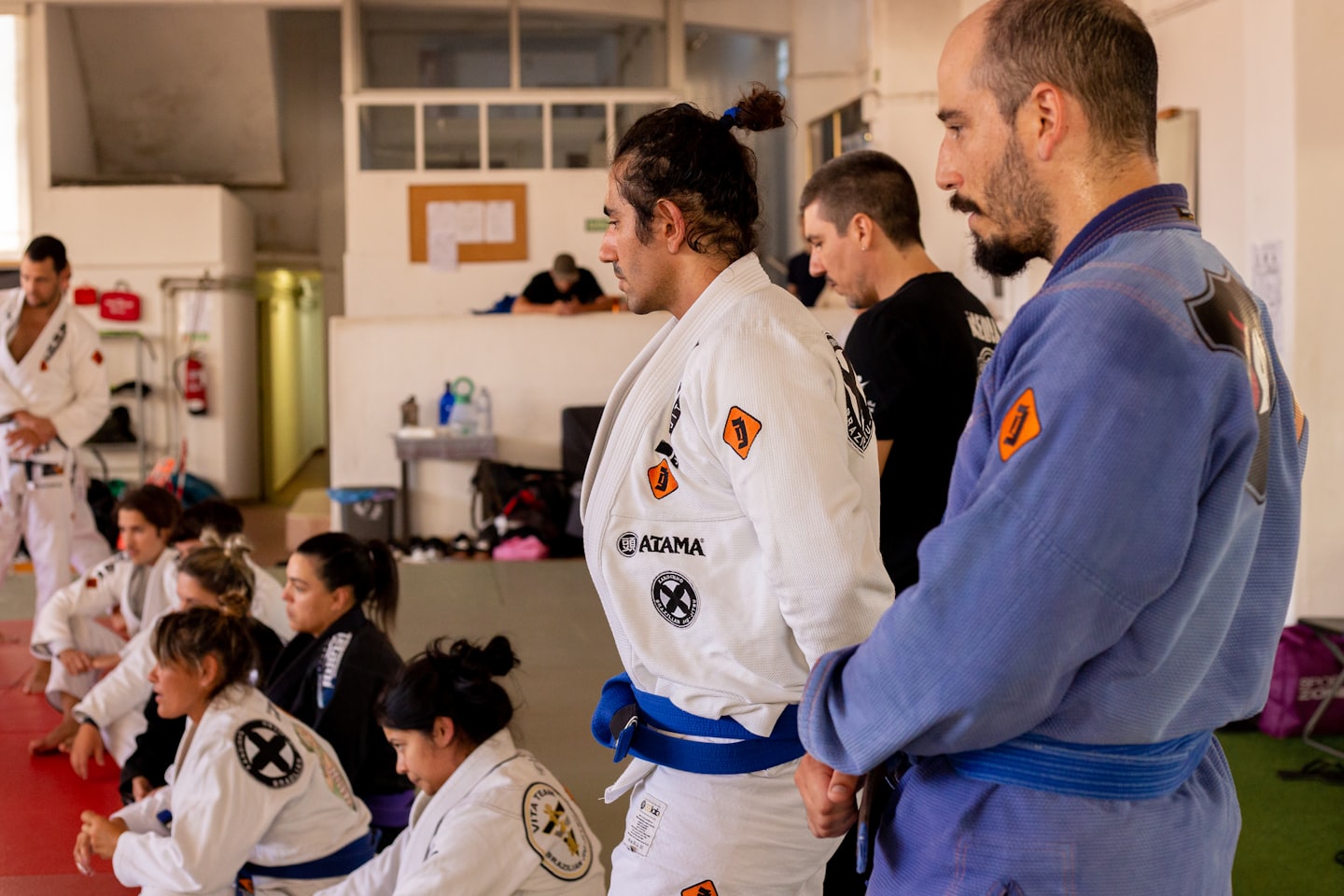 Erwachsene in Gis praktizieren brasilianisches Jiu-Jitsu in einer Turnhalle.