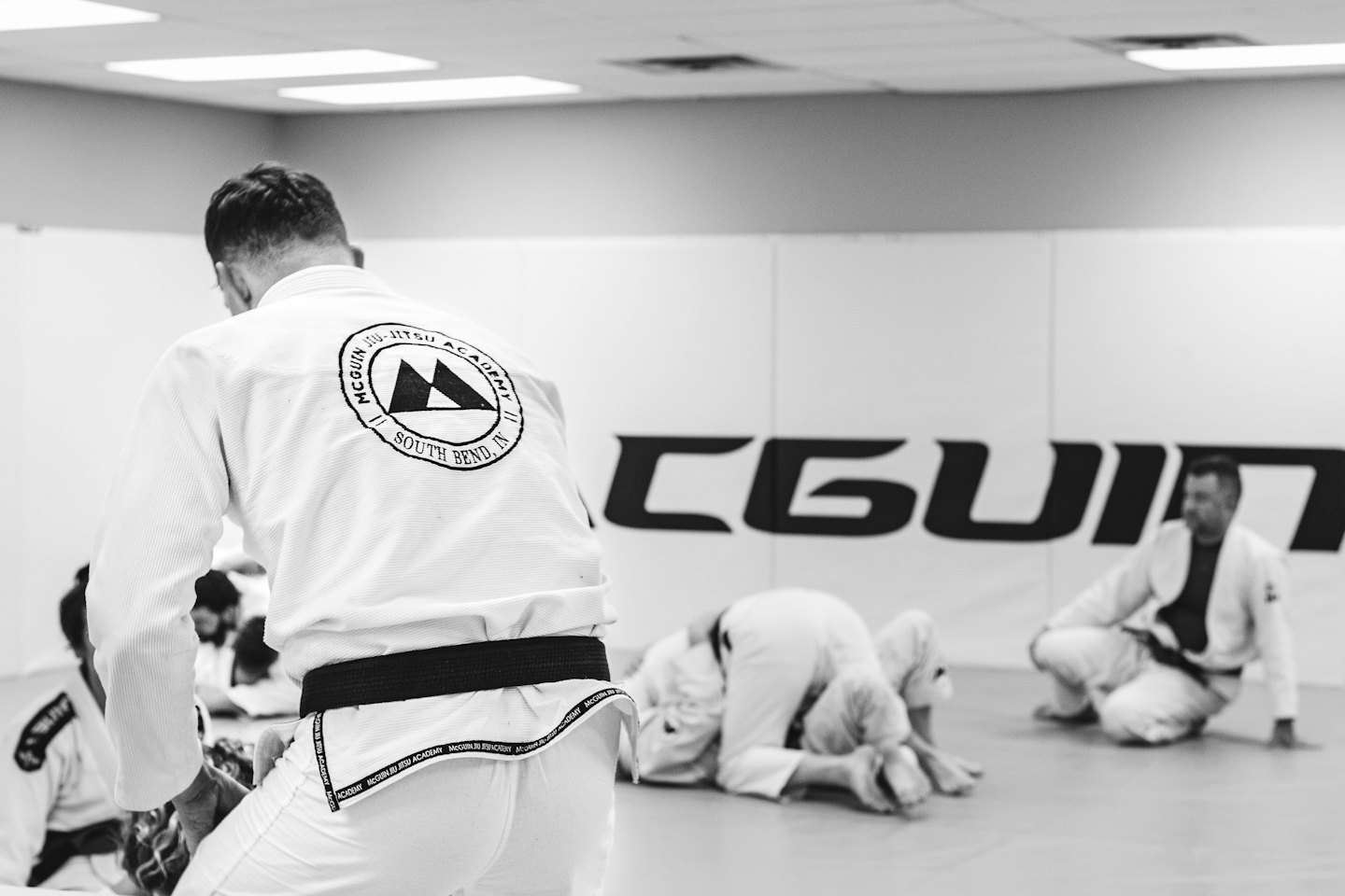 Leute praktizieren brasilianisches Jiu-Jitsu auf Matten in einer Turnhalle.