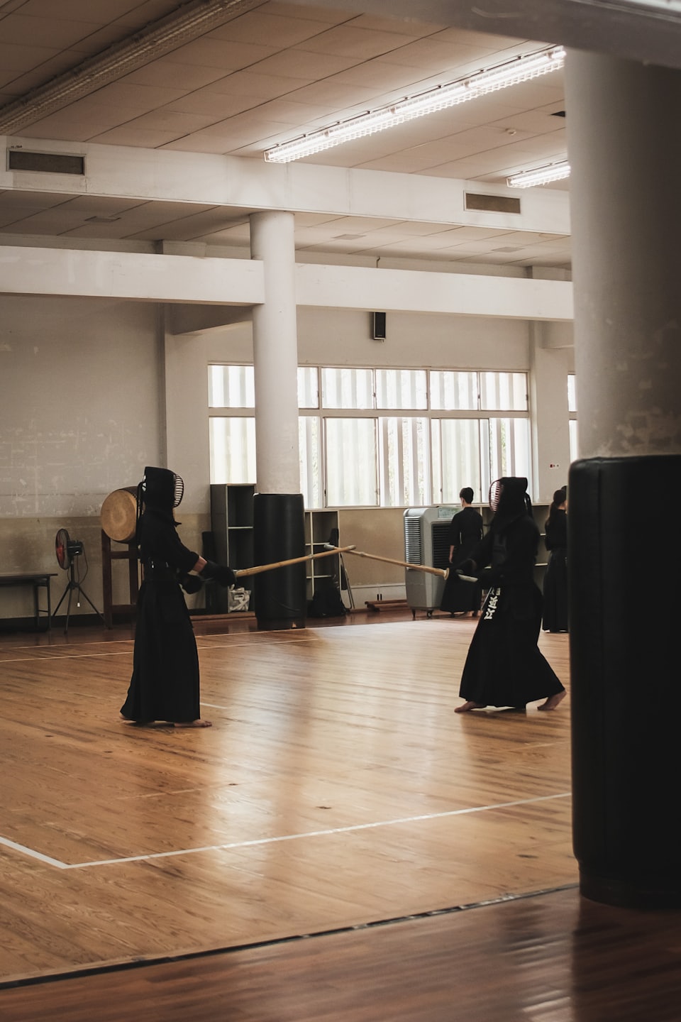 Zwei Kendo-Praktizierende duellieren sich mit Shinai auf einem Fitnessboden.