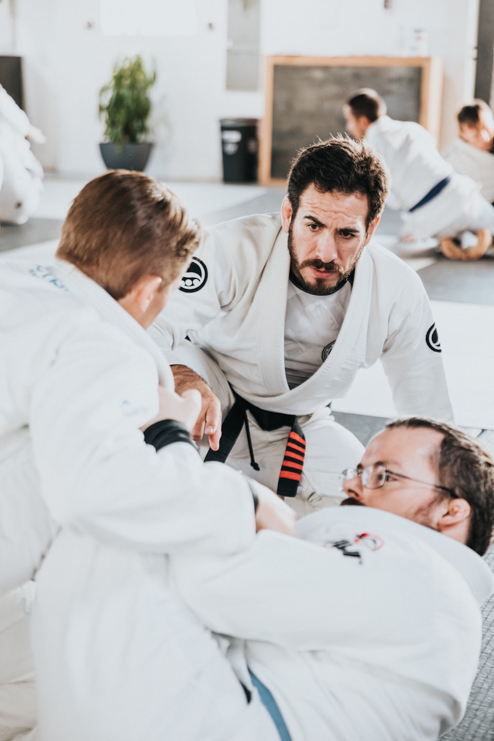 Bärtiger Lehrer beobachtet Schüler beim brasilianischen Jiu-Jitsu auf Matten.